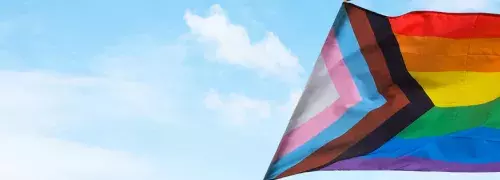a progress pride flag in front of a blue sky